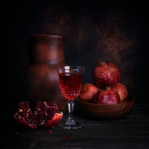 A stylish composition featuring pomegranates, a wine glass, and a rustic jug on a dark background.